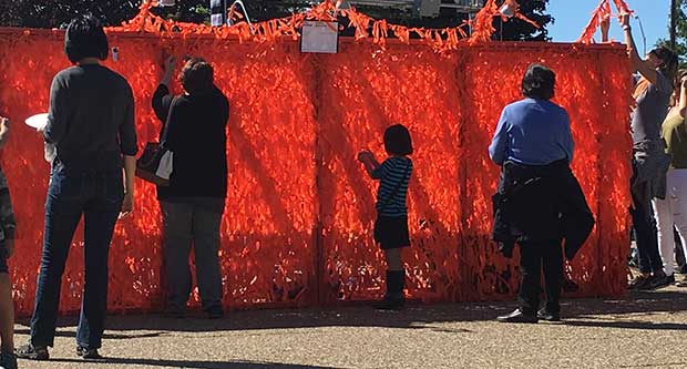 Orange ribbons being tied onto Color Me Orange—Color Me Kind at ArtPrize Eight